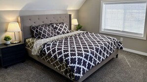 Une chambre à coucher avec un lit, deux tables de chevet, une lampe et une fenêtre avec des stores.