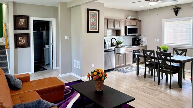 Un salon moderne comprenant un canapé, une table à manger avec des chaises, un coin cuisine avec des placards et des appareils électroménagers, et un ventilateur de plafond.