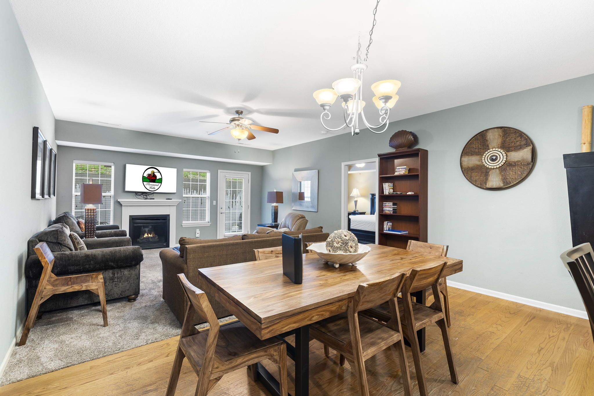 Un salon spacieux avec une cheminée, un coin repas avec une table et des chaises en bois, et un ventilateur de plafond.