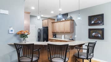 A kitchen with wooden cabinets, a central island with bar stools, pendant lighting, and two framed artworks on the wall.