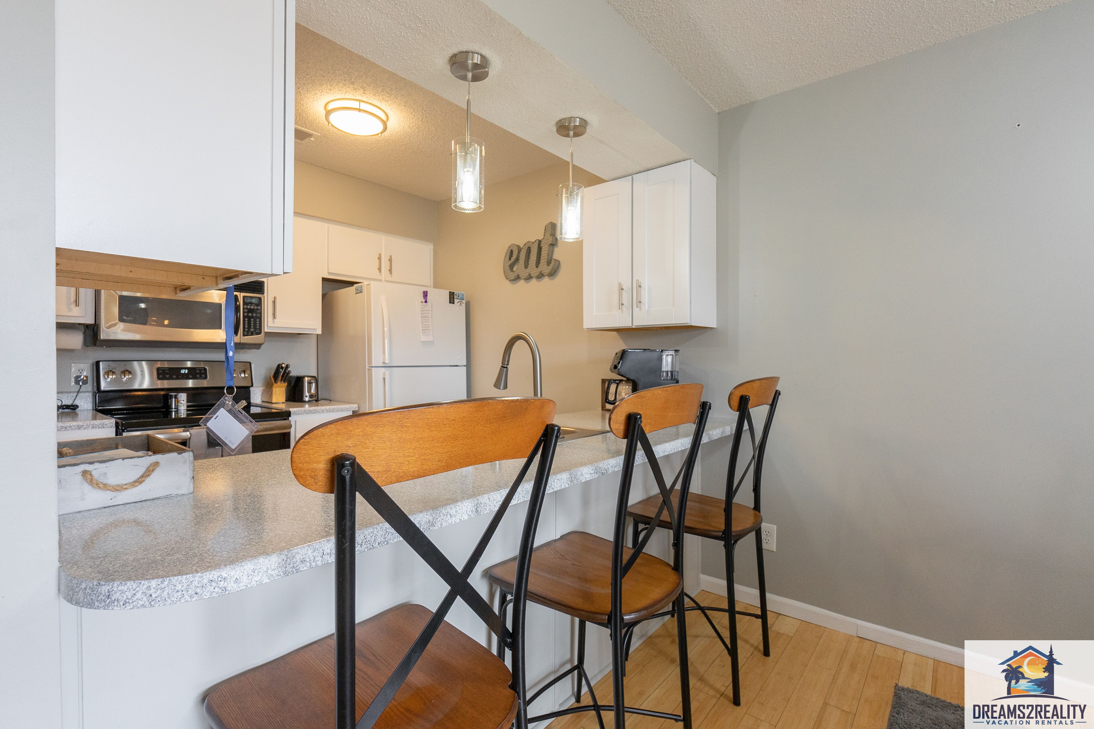 A modern kitchen with white cabinets, a microwave, a refrigerator, and a bar area with stools.