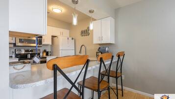 A modern kitchen with white cabinets, a microwave, a refrigerator, and a bar area with stools.