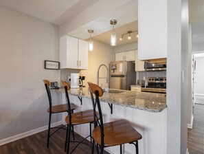 Cozinha moderna com bancadas de granito, eletrodomésticos de aço inoxidável e um espaço de bar com banquetas.