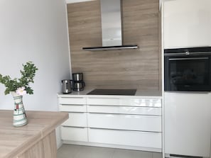 Eine moderne Küche mit weißen Schränken, einer Edelstahl-Dunstabzugshaube, einem Einbauofen und einer Kaffeemaschine auf der Arbeitsplatte.