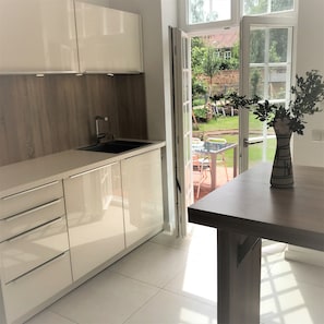 Eine moderne Küche mit weißen Schränken, einer schwarzen Spüle und Blick auf einen Garten durch eine geöffnete Tür.