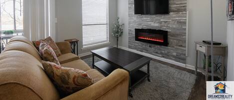 Una sala de estar con sofá, mesa de centro, chimenea, televisor y lámpara.