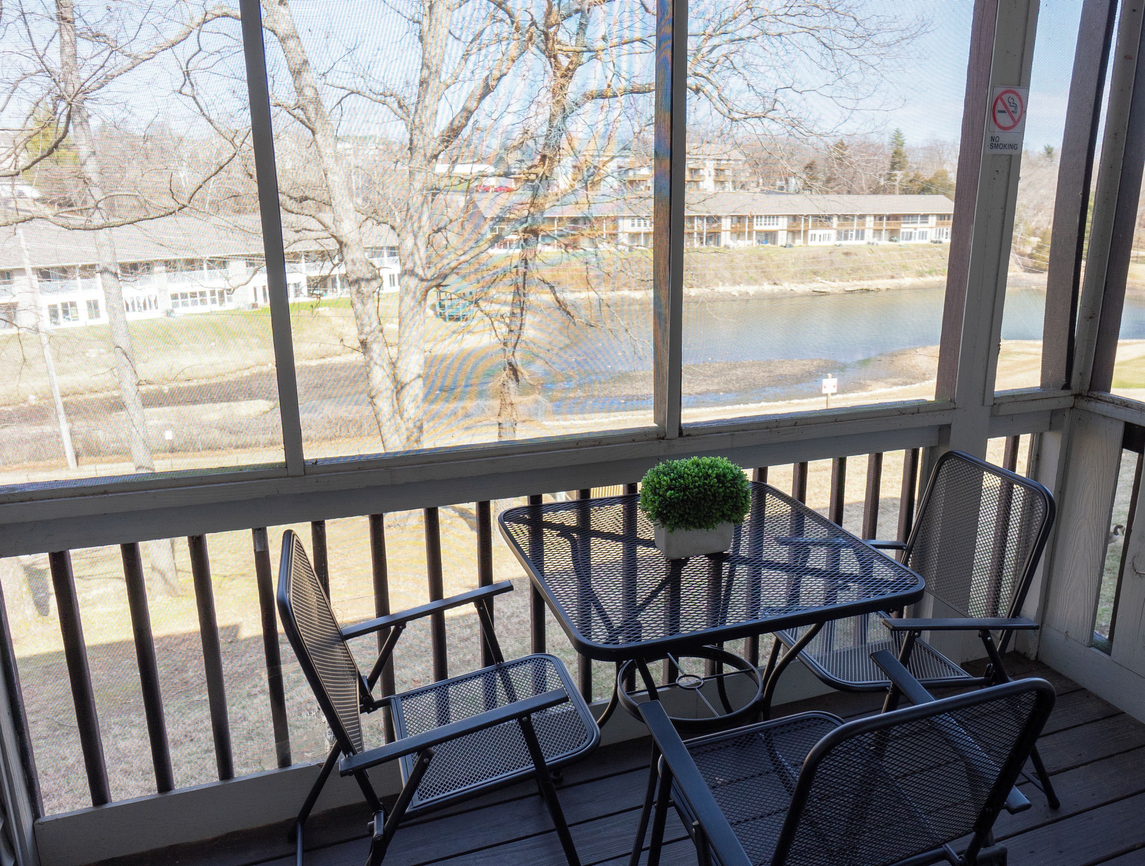 Un espace extérieur abrité, avec une table et des chaises, d’où l’on peut admirer un plan d’eau et des bâtiments en arrière-plan.