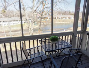 A covered outdoor seating area with a table and chairs, overlooking a body of water and buildings in the background. - 1BR WALK-IN~Pet Friendly ~ Resort Amenities ~ Fishing ~ FREE TICKETS INCLUDED! (PR40-10) (Branson)