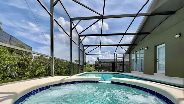 A covered outdoor swimming pool with a glass ceiling, surrounded by a green fence and a house in the background. - Private Pool & Spa • Game Room • 2 King Ensuites • 15 Minutes to Disney (Clermont)