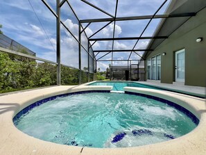 A covered outdoor swimming pool with a glass ceiling, surrounded by a green fence and a house in the background. - Private Pool & Spa • Game Room • 2 King Ensuites • 15 Minutes to Disney (Clermont)