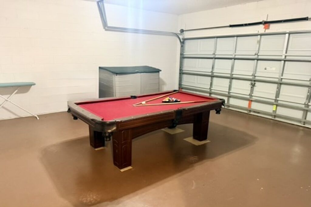 Una mesa de billar en una habitación con una puerta de garaje, una silla plegable y un módulo de almacenamiento.