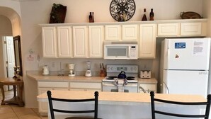 A kitchen with white cabinets, a microwave, a stove, and two black chairs. - Private Pool & Spa • Game Room • 2 King Ensuites • 15 Minutes to Disney (Clermont)