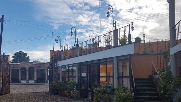 A courtyard with cobblestone flooring, a building with a glass entrance, and potted plants. - Villas Tonantzintla (San Andrés Cholula)