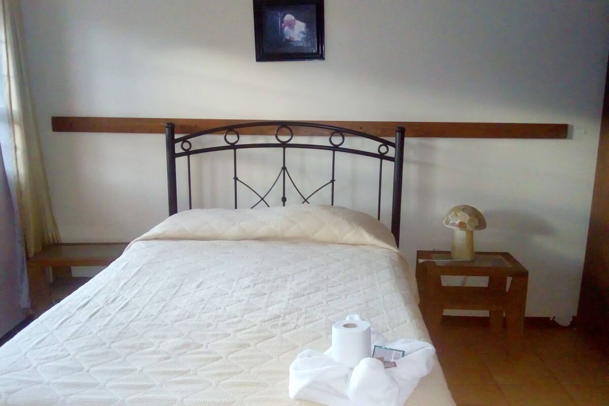A neatly made bed with a quilted mattress, a wooden headboard, and a small bedside table with a lamp and a decorative object.
