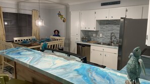Uma cozinha moderna com armários brancos, bancada de mármore e geladeira de aço inoxidável.