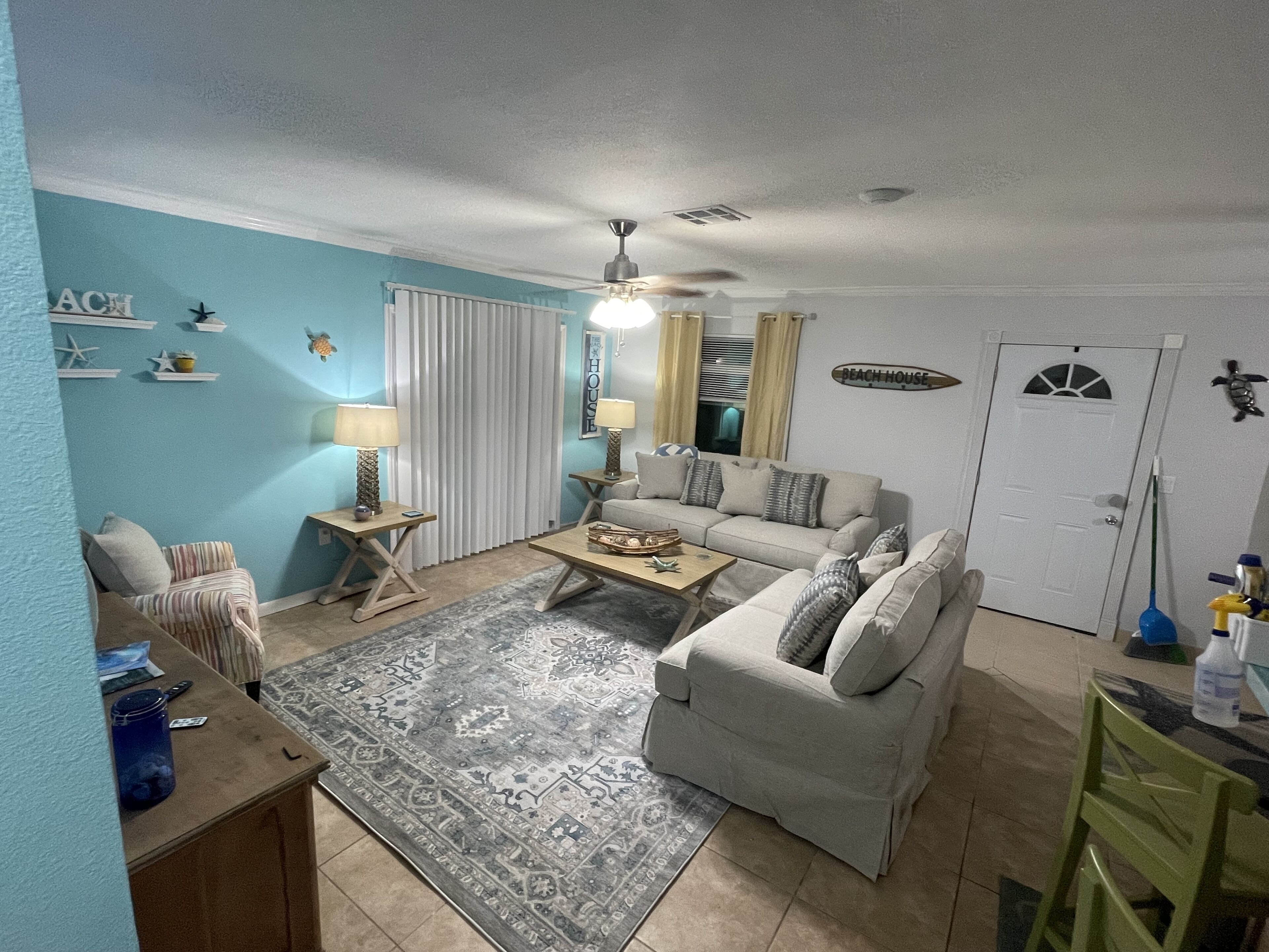 A living room with a sofa, two side tables, a coffee table, a patterned rug, and a ceiling fan.