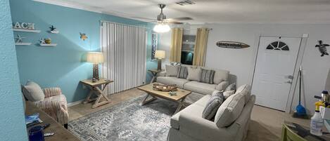 A living room with a sofa, two side tables, a coffee table, a patterned rug, and a ceiling fan.