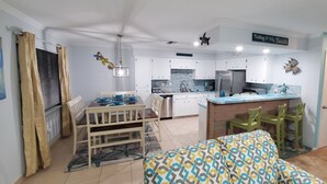 Cozinha compacta com armários brancos, geladeira de aço inoxidável e um pequeno espaço de jantar com mesa e cadeiras.