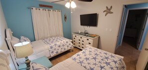 A bedroom with two beds, a TV, a dresser, and a ceiling fan. - WALK TO BEACH ACCESS! DOG FRIENDLY! UNIT 2A (Englewood)