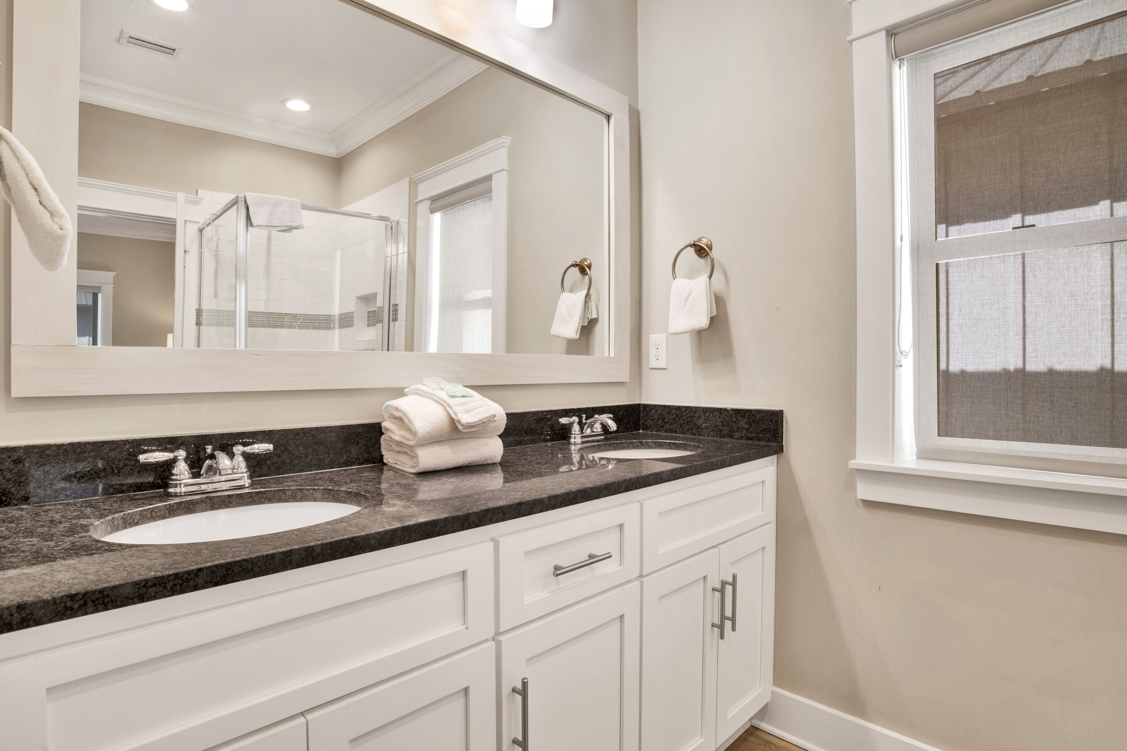 A bathroom with two sinks, a large mirror, and a window with a view.