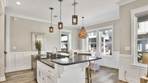 A spacious kitchen with a large island, pendant lighting, and a view of the backyard through large windows.