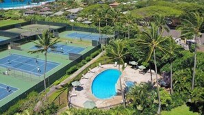 Een tenniscomplex met meerdere banen, een zwembad en weelderige groene beplanting.