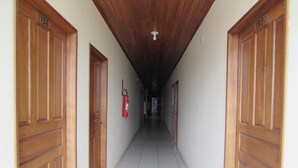 A hallway with wooden doors numbered 13B and 135, white tiled floor, and a fire extinguisher on the wall. - Hotel Trevo (Boa Vista)
