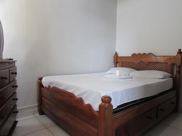 A wooden bed with a white bedspread, a wooden headboard, and a wooden dresser with multiple drawers.