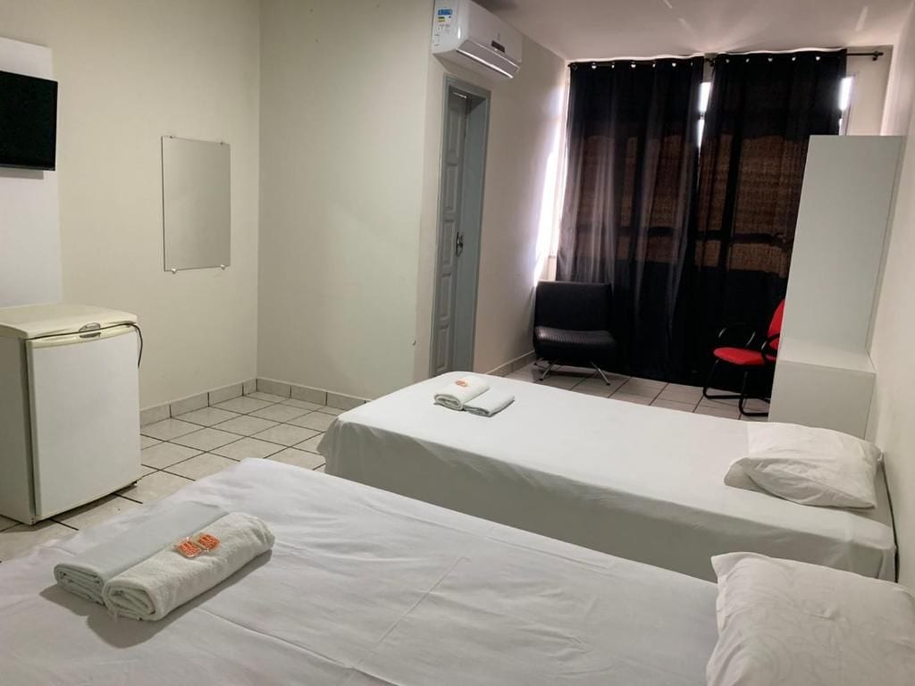 Quarto de hotel com duas camas, uma escrivaninha, uma cadeira e vista para o exterior.