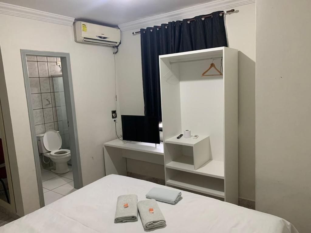 Habitación de hotel con cama, escritorio con computadora, armario, baño con inodoro y aire acondicionado.