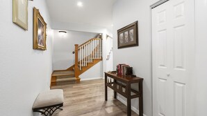 A hallway with a wooden staircase, a bench, a table with books, and framed pictures on the walls. - Gated 5BR Retreat • Private Patio • Sleeps 12 • Pool • Near Shows, Golf & Dining (Branson)