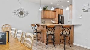 A modern kitchen with wooden cabinets, a central island with bar stools, pendant lighting, and a decorative wall piece. - Gated 5BR Retreat • Private Patio • Sleeps 12 • Pool • Near Shows, Golf & Dining (Branson)