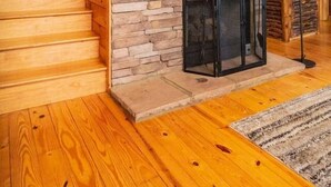 Eine Holztreppe führt zu einem Raum mit einer Steinwand, einem Kamin und einem Fernseher.