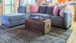 Ein gemütliches Blockhauss-Interieur mit Holzbalkendecke, einer Eckcouch, einem kleinen Tisch und einem Teppich.