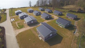 A row of modern, single-story cabins with a flat roof, arranged in a linear fashion along a paved road, adjacent to a large body of water.