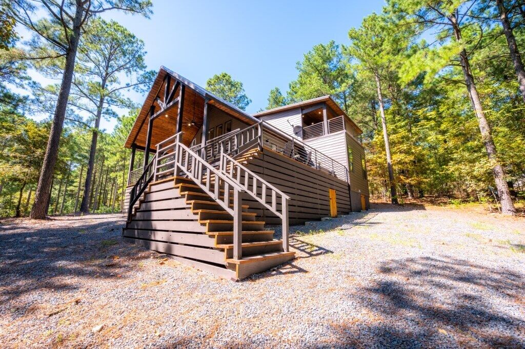 A cabin with a wooden staircase leading to a deck, surrounded by trees.