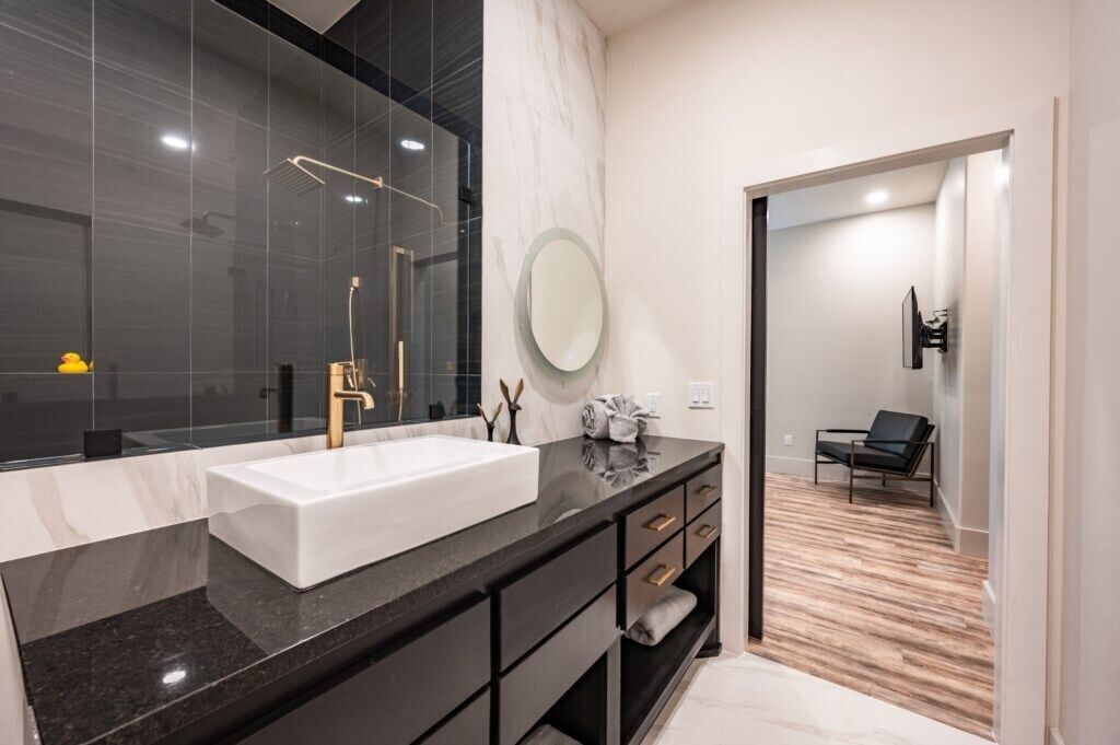 A modern bathroom with a large mirror, a white sink, and a black vanity.
