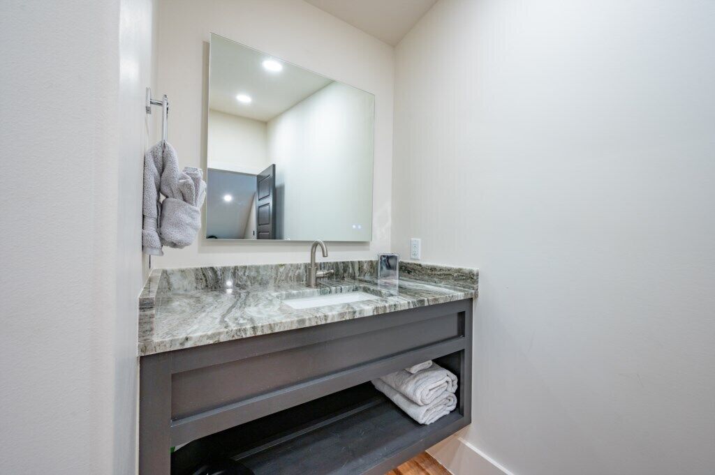 Un baño con lavamanos de mármol, un espejo grande y un perchero para toallas.