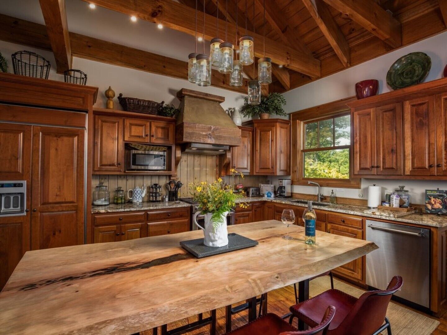 A kitchen with wooden cabinets, a granite countertop, a central island with a vase of flowers, and hanging light fixtures.