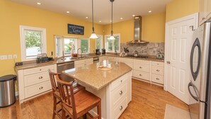 A modern kitchen with a large island, white cabinetry, and a yellow accent wall. - Deep Creek Escape w/ Dock, Hot Tub & Views (Oakland)