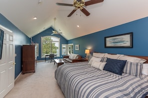 A bedroom with a large bed, a ceiling fan, and a view of the outdoors.