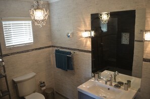 Een badkamer met toilet, wastafel en douche. Twee kroonluchters en een handdoekrek met een blauwe handdoek.