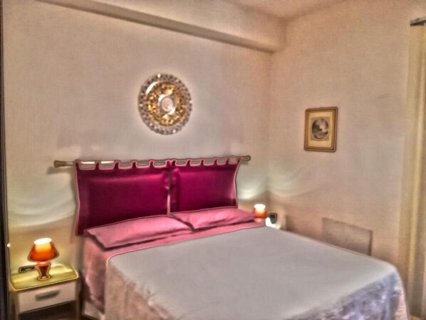 A bedroom with a bed, a nightstand, a lamp, a decorative wall piece, and a framed picture. - SEGESTA - New Nouveau Bedding (Salemi)