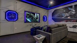 Ein modernes Wohnzimmer mit grauem Sofa, einem weißen Beistelltisch und einem großen Flachbildfernseher an der Wand.