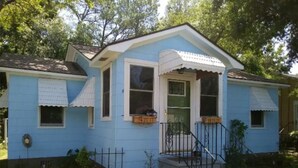 Ein eingeschossiges Haus mit blauer Fassade, weißer Verkleidung, einer Veranda mit Geländer und einem kleinen Vorgarten.