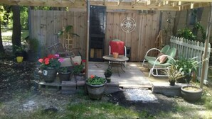 Eine hölzerne Pergola mit Tisch und Stühlen, umgeben von Topfpflanzen und einem weißen Ziergartenzaun.