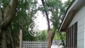 Un cancello di legno con un cartello, un elemento decorativo in metallo sopra e un piccolo giardino con piante.