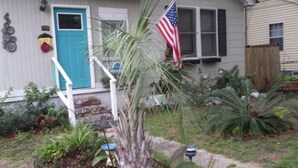 Una casa con una porta blu, una bandiera americana e un piccolo giardino con diverse piante.