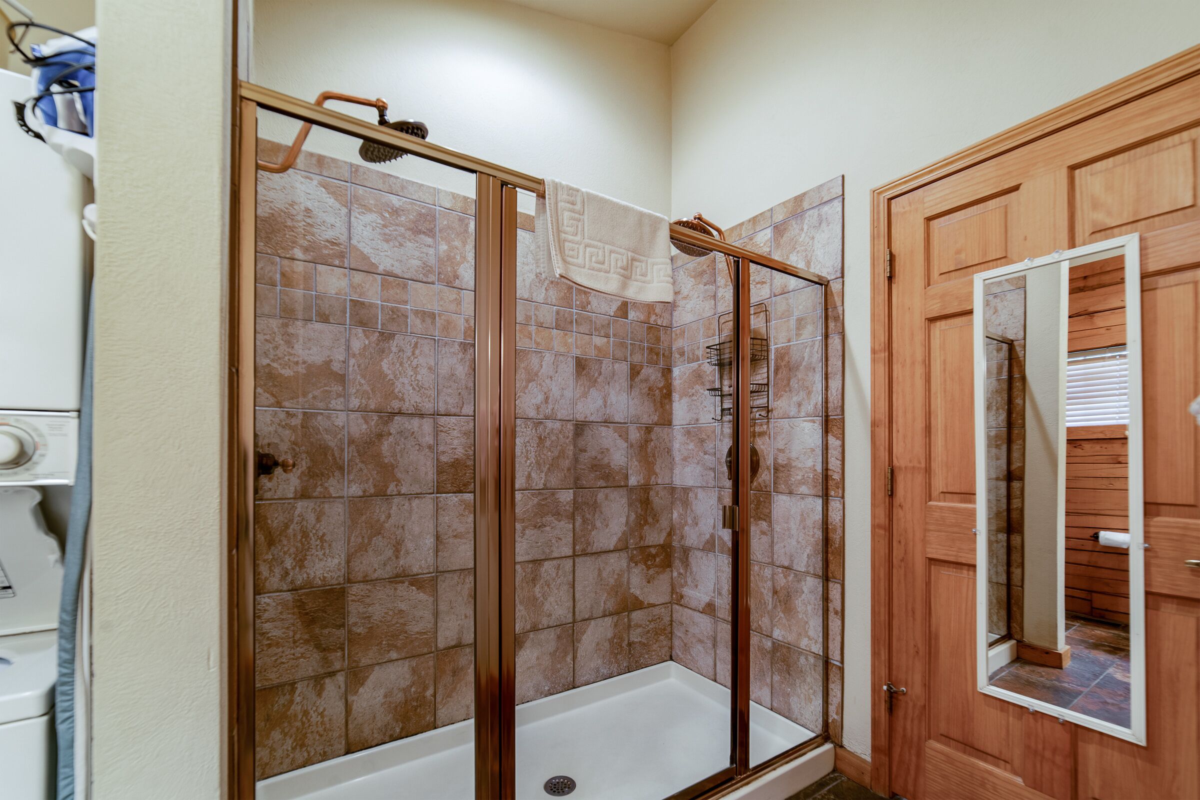 A shower area with a glass door, tiled walls, and a wooden door with a mirror.