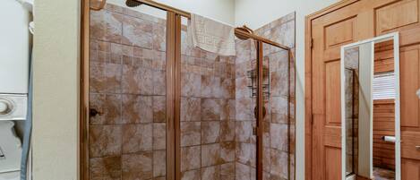 A shower area with a glass door, tiled walls, and a wooden door with a mirror.